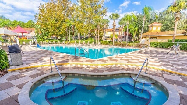 A swimming pool with a checkered tile pattern, surrounded by lounge chairs and palm trees. - Encantada Resort Townhome with Pool Near Disney (Kissimmee)