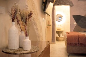 Ein Zimmer mit einem Bett, einem kleinen Tisch und zwei Vasen mit getrockneten Blumen auf einer Glastischplatte.