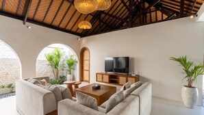 A modern living room with a sofa set, wooden coffee table, TV, and potted plants. - Jimbaran Bay Villas (Kedonganan)