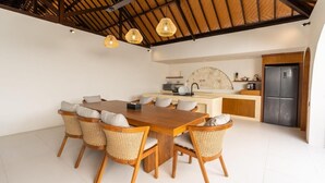 A modern kitchen with a central island, a dining area with a wooden table and wicker chairs, and a large refrigerator. - Jimbaran Bay Villas (Kedonganan)