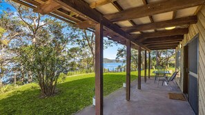 A covered outdoor area with a concrete floor, wooden beams, and a view of a body of water and hills in the background. - The Treehouse on Hardys by HolidayCo. (KILLCARE)