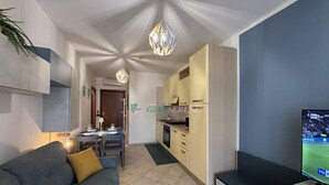 A modern living room with a grey sofa, a dining area with a table set for four, a kitchen with light-colored cabinets, and a TV on a stand. - 5 bed places with swimming pool in the area Coop (Toscana)