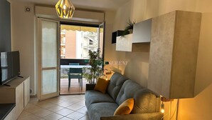 A modern living room with a sofa, a TV, a pendant light, and a view of a balcony with a table and chairs. - 5 bed places with swimming pool in the area Coop (Toscana)