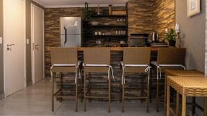 Une cuisine compacte équipée d’un réfrigérateur, de tabourets de bar et d’une petite table à manger.