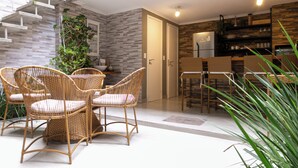 Une cuisine moderne dotée d’un réfrigérateur encastré, un coin repas avec des chaises en osier et un escalier agrémenté d’une plante.