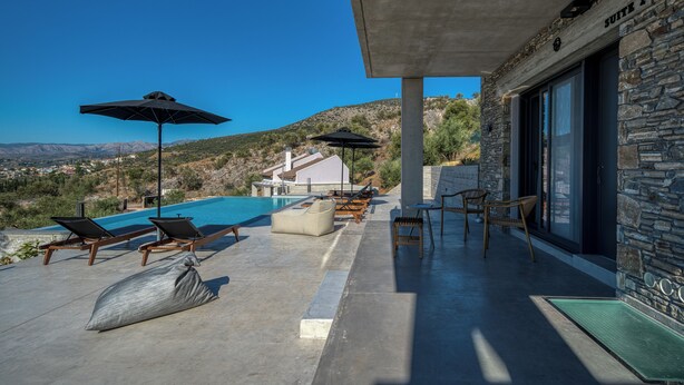 A modern outdoor pool area with lounge chairs and umbrellas, a stone wall, and a view of the landscape.