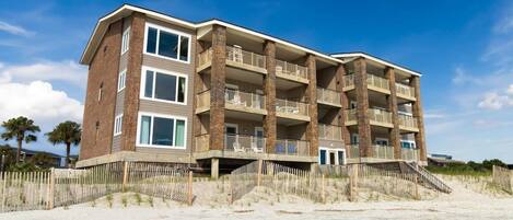 A multi-story hotel with balconies, located near a sandy beach.