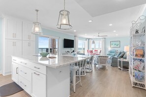 Une cuisine spacieuse avec des meubles blancs, un grand îlot central et des luminaires suspendus.