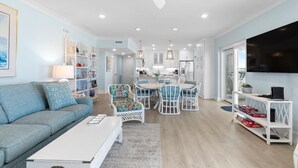 A modern living room with a sofa, coffee table, and a dining area with chairs and a table. - Beachfront Bliss: 3 Bdrm 1st Flr (Pawleys Island)