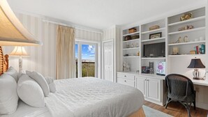 Un dormitorio con cama, escritorio, estanterías y ventana con cortinas.