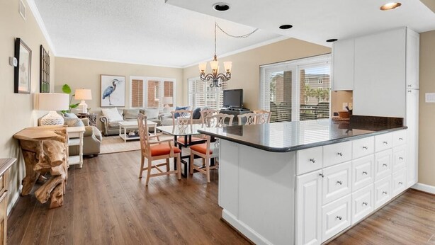 A spacious kitchen with a central island, white cabinetry, and a dining area with wooden chairs. - Perfectly Poised 2 Bedroom Oceanview 2nd Flr (Pawleys Island)