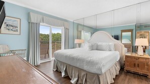 A bedroom with a large bed, a wooden nightstand, a mirror, and a view of the outdoors through a sliding door. - Perfectly Poised 2 Bedroom Oceanview 2nd Flr (Pawleys Island)