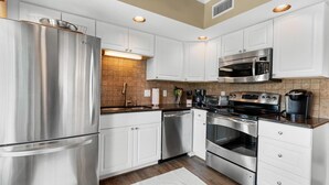 A modern kitchen with stainless steel appliances, white cabinetry, and a tiled backsplash. - Perfectly Poised 2 Bedroom Oceanview 2nd Flr (Pawleys Island)