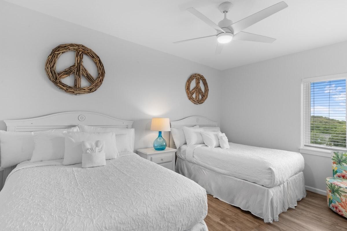 A bedroom with two beds, a ceiling fan, and a window with blinds.