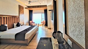 Habitación de hotel con cama, cafetera, dos tazas, bandeja y vista al mar.