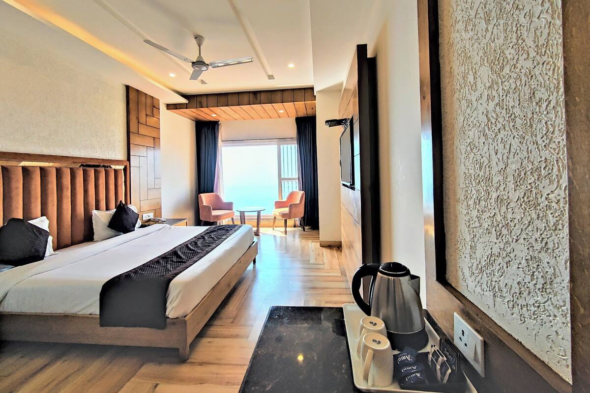 Une chambre d’hôtel avec un lit, une machine à café, deux tasses, un plateau et une vue sur la mer.