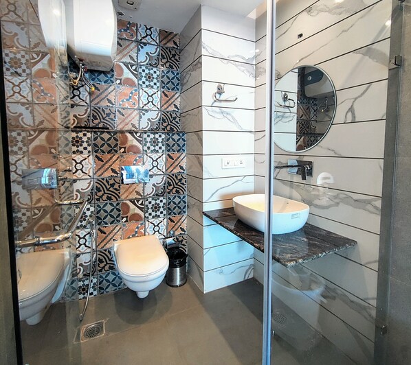 A modern bathroom with patterned tiles, a white toilet, a sink with a marble countertop, and a glass shower enclosure. - Luxury Inn by Stotrak Hotels (Mussoorie)
