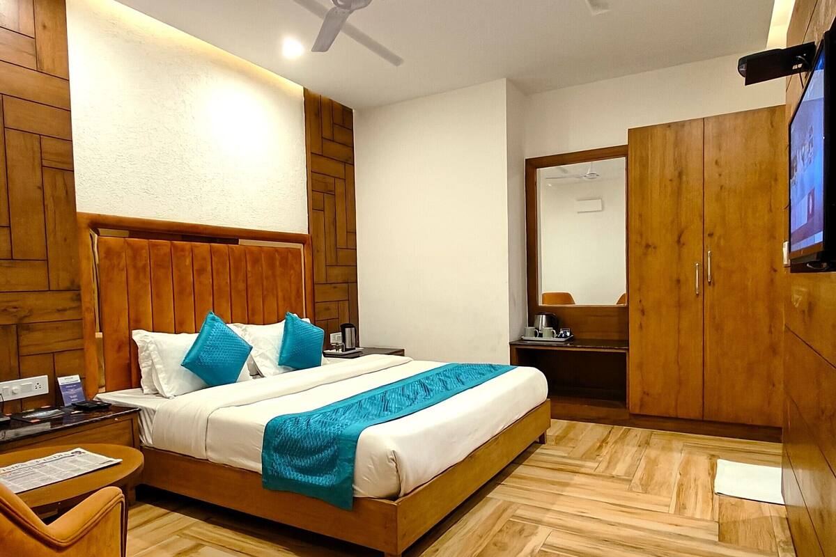Une chambre d’hôtel moderne avec une tête de lit en bois, un lit avec une literie bleue, un plancher en bois, un ventilateur de plafond, une télévision et une armoire.