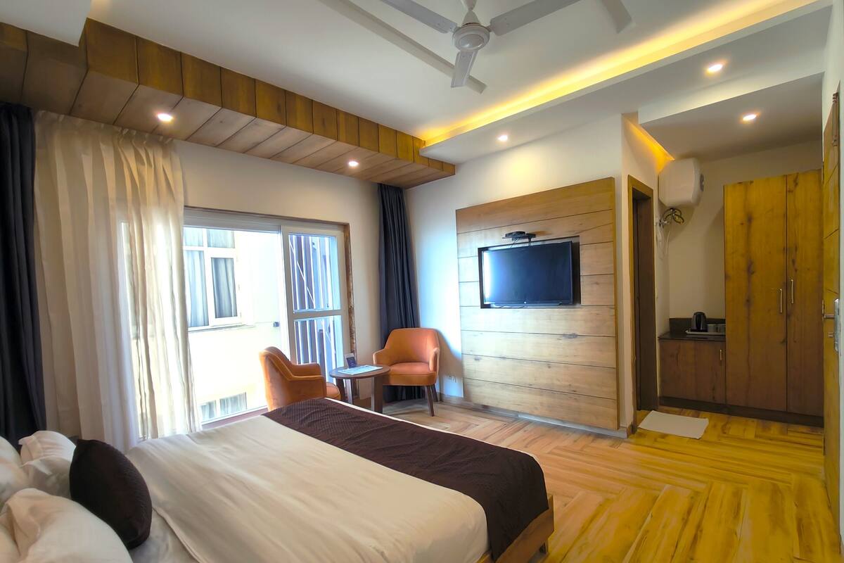 Une chambre d’hôtel moderne dotée d’un grand lit, d’un téléviseur fixé à un mur en bois, d’une petite table avec une chaise et d’un coin cuisine.