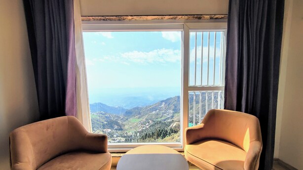 Una habitación con dos sillones y una mesita, un ventanal con vistas a un paisaje montañoso.