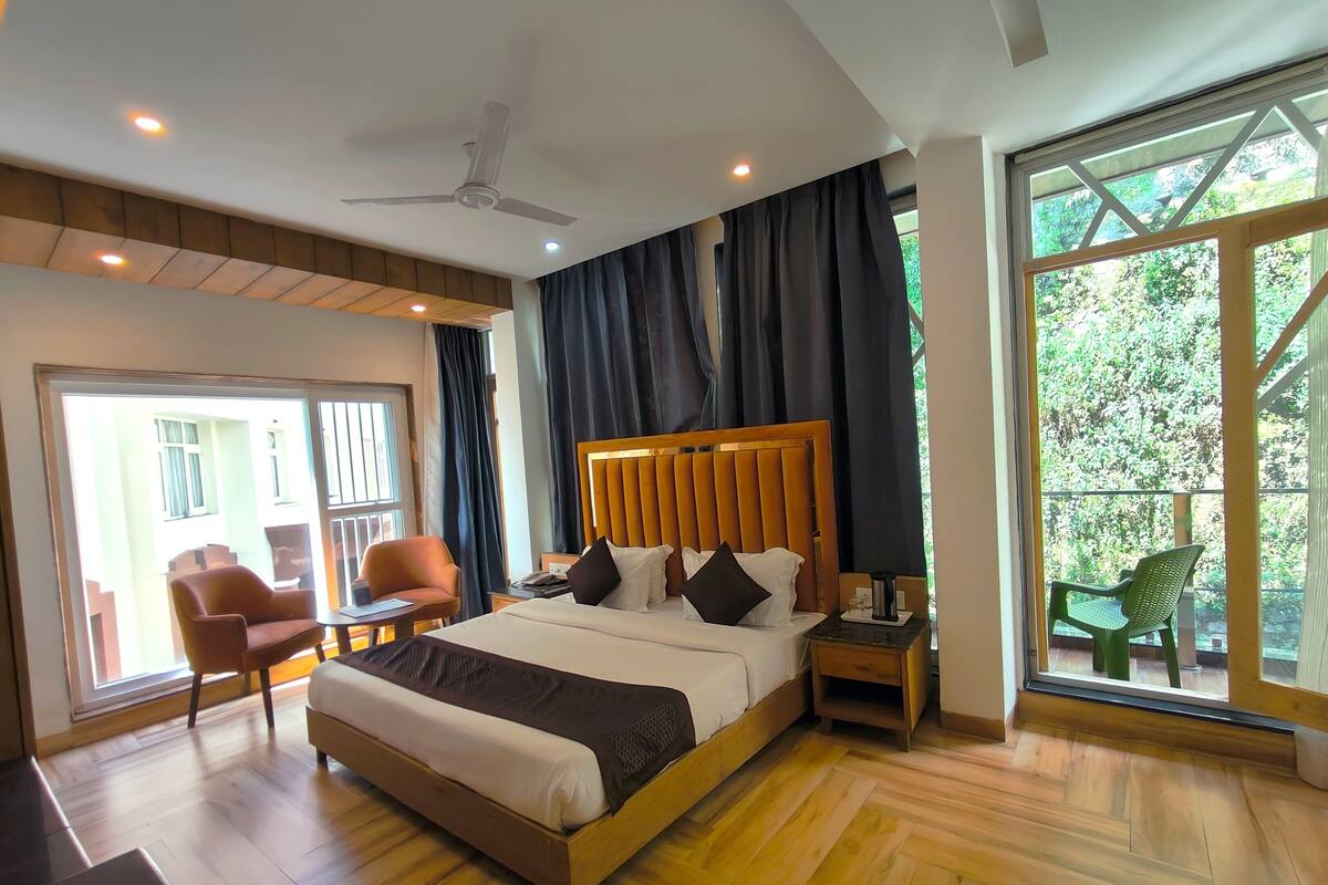 Une chambre d’hôtel moderne avec un grand lit, une tête de lit en bois et une vue sur la verdure par la fenêtre.