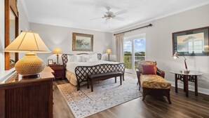 A bedroom with a bed, a bench, a chair, a desk, and a ceiling fan.
