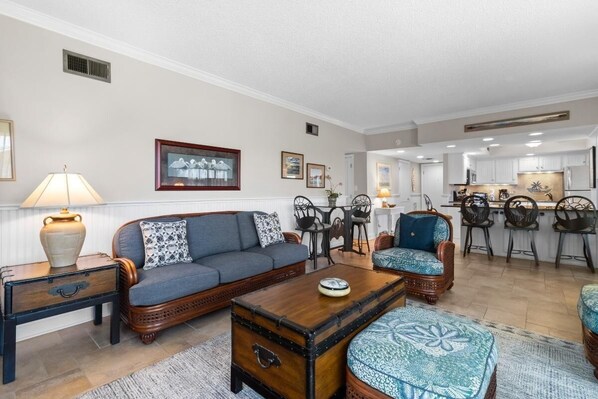 A living room with a sofa, armchairs, a coffee table, and a dining area with chairs and a table. - Brilliant 2 Bdrm Oceanview 2nd Flr (Pawleys Island)