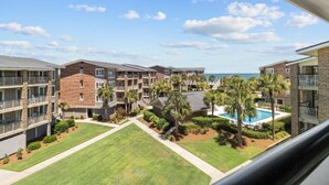 A multi-story residential building with balconies, a swimming pool, and a view of the ocean.