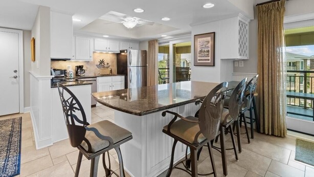 A modern kitchen with white cabinetry, a central island with bar stools, and a ceiling fan.