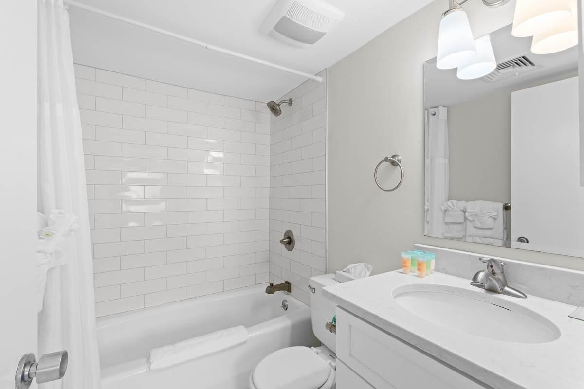 A modern bathroom with white tiles, a bathtub, a toilet, a sink, and a mirror.