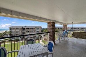 Un balcon avec une table et des chaises, donnant sur une plage et un quartier résidentiel.