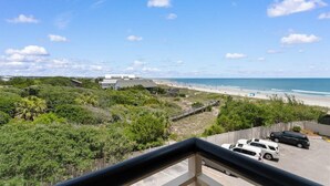 Une vue sur la côte depuis un balcon donnant sur une plage où sont garées des voitures, avec un ciel dégagé.