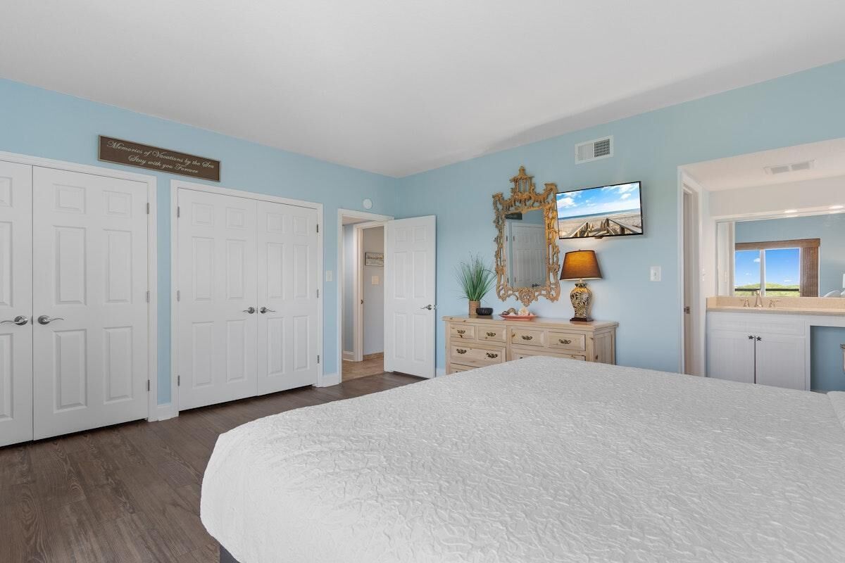 Un dormitorio con una cama grande, un aparador, un espejo y una puerta que da a otra habitación.