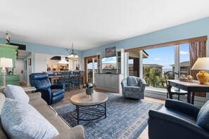 A spacious living room with a blue sofa, a coffee table, and a dining area with a table and chairs. - It's Time for the Beach: 3 Bdrm Oceanview 4th Flr (Pawleys Island)