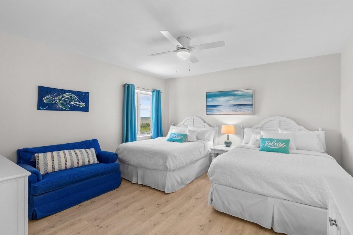 Ein Zimmer mit zwei Betten, einem blauen Sofa, einem Deckenventilator und Bildern an den Wänden.
