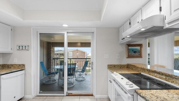 A modern kitchen with a built-in stove, white cabinets, and a sliding glass door leading to a balcony with outdoor seating.