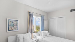 Une chambre d’hôtel avec deux lits, une fenêtre avec des rideaux, un tableau encadré au mur et une armoire.