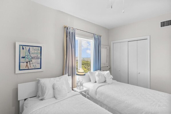 A hotel room with two beds, a window with curtains, a framed picture on the wall, and a wardrobe.