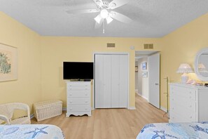 A bedroom with a bed, a dresser, a television, a wardrobe, a ceiling fan, and a door leading to another room. - Beach, Sun and Golf: 3 Bdrm Oceanview 4th Flr (Pawleys Island)