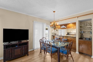 A dining area with a TV, wooden chairs, a glass table, and a chandelier.