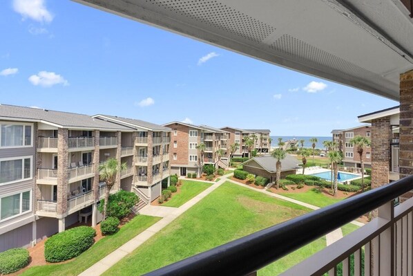 A multi-story residential building with balconies, a swimming pool, and a clear view of the ocean.