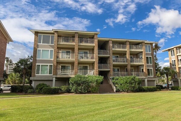 A multi-story residential building with balconies, a central staircase, and a well-maintained lawn.