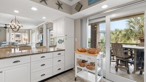 A kitchen with white cabinets, a granite countertop, and a view of the outdoor patio. - 3rd Flr, 3 Bdrm Oceanview Condo Beach Oasis (Pawleys Island)