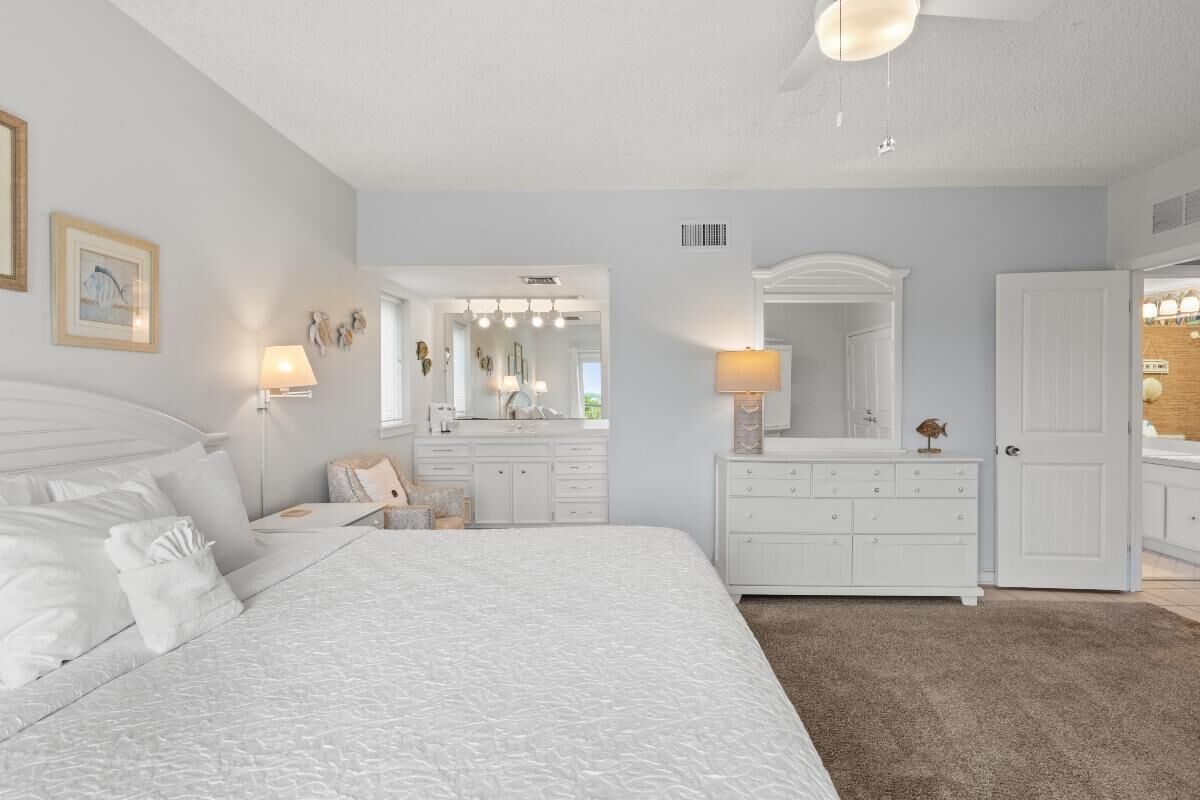 A bedroom with a large bed, a dresser, a mirror, and a door leading to another room.