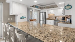 A modern kitchen with white cabinets, granite countertops, stainless steel appliances, and a clock on the wall. - 3rd Flr, 3 Bdrm Oceanview Condo Beach Oasis (Pawleys Island)