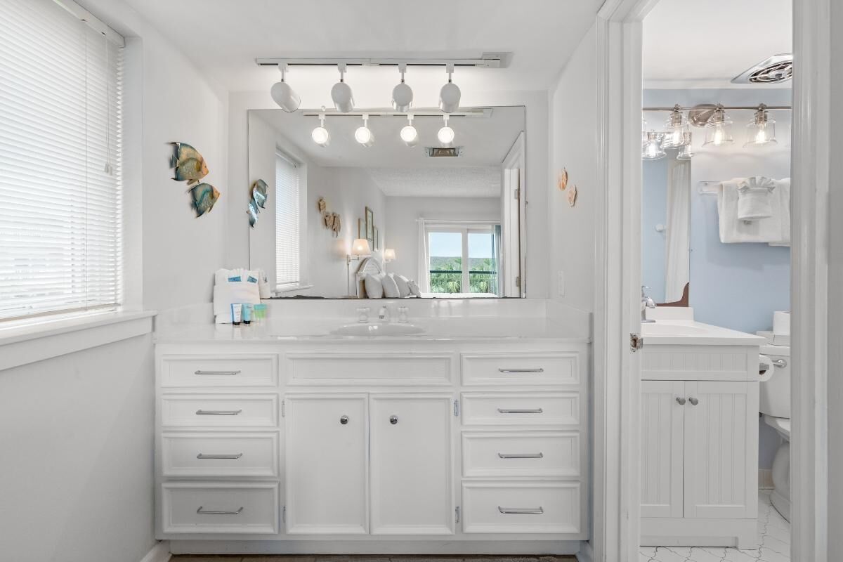 Een moderne badkamer met een groot wit badkamermeubel, een spiegel met verlichting en uitzicht op het landschap.