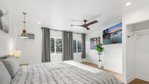 A bedroom with a bed, a ceiling fan, a window with curtains, a wall-mounted air conditioner, and a painting. - Zephyr Cove Studio Unit 6 (Zephyr Cove)