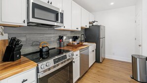 A modern kitchen with white cabinets, a stainless steel range, a microwave, a kettle, and a coffee maker. - Zephyr Cove Studio Unit 6 (Zephyr Cove)