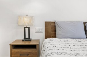 Una cama bien hecha con una colcha estampada, una mesita de noche con lámpara y un cabecero de madera.
