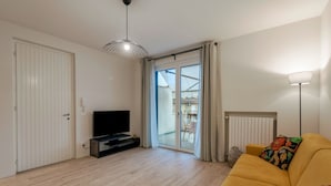 A living room with a sofa, a TV, a lamp, and a sliding glass door leading to a balcony. - Attilia House - with WiFi and air conditioning (Sirmione)